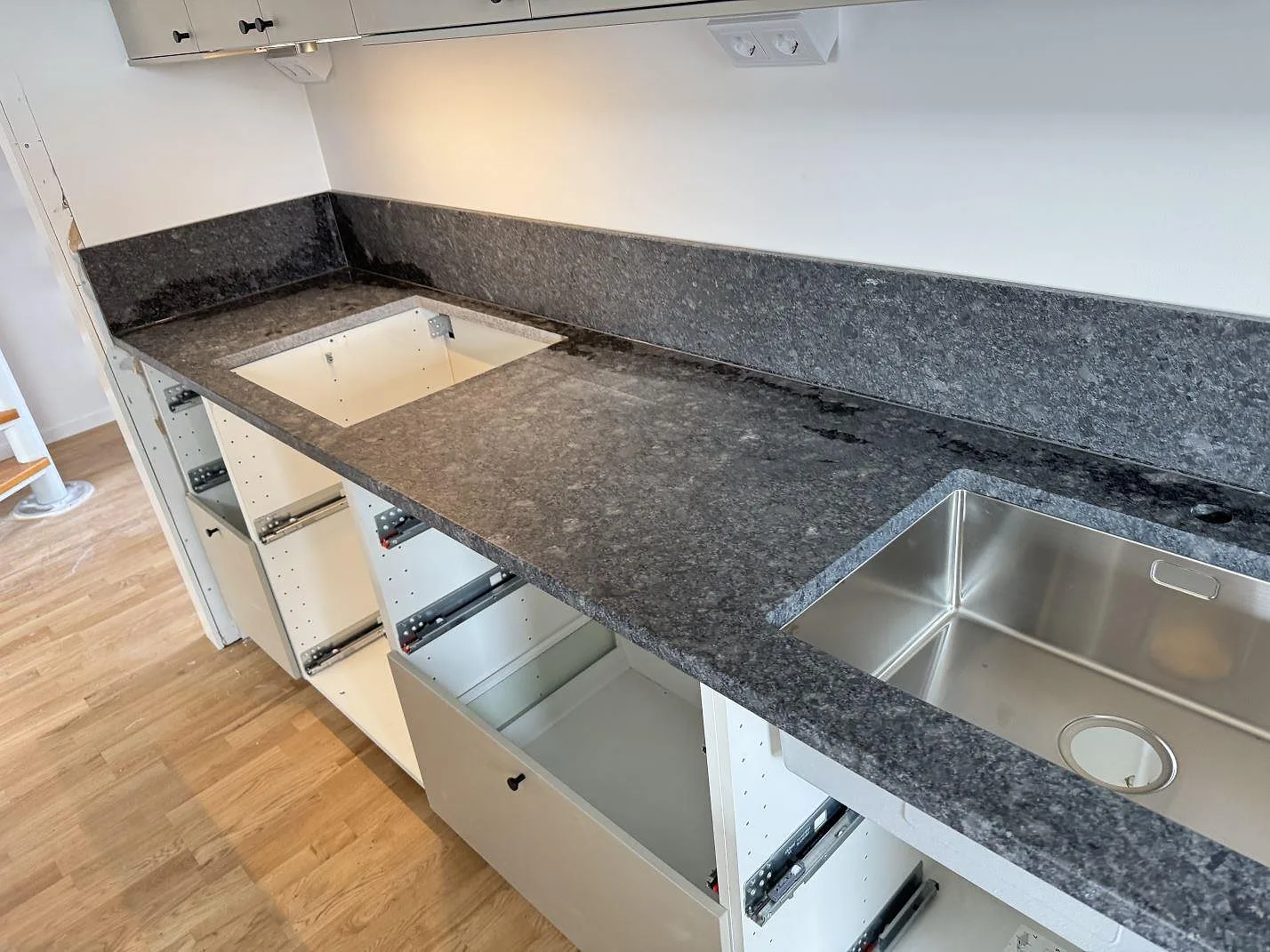 Lång köksbänkskiva i Steel Grey granit med lädermatt yta, diskho, hällurtag och uppvikt stänkkant i Bjärred.