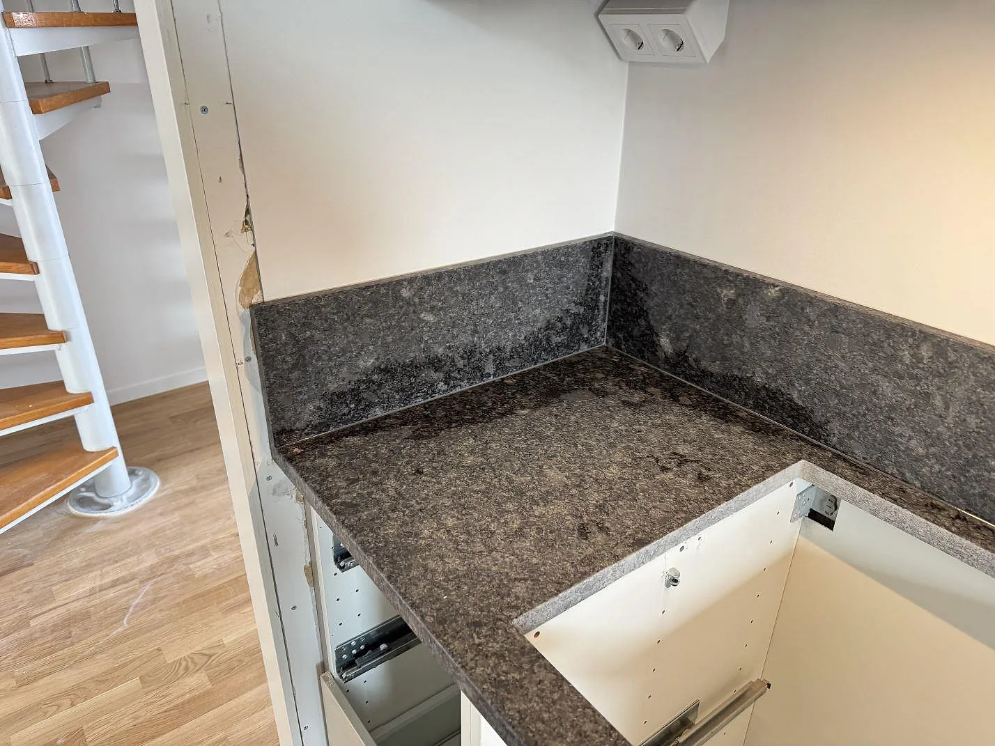 Hörnparti med Steel Grey granit, lädermatt bänkskiva och uppvikt stänkkant i ett kök i Bjärred.