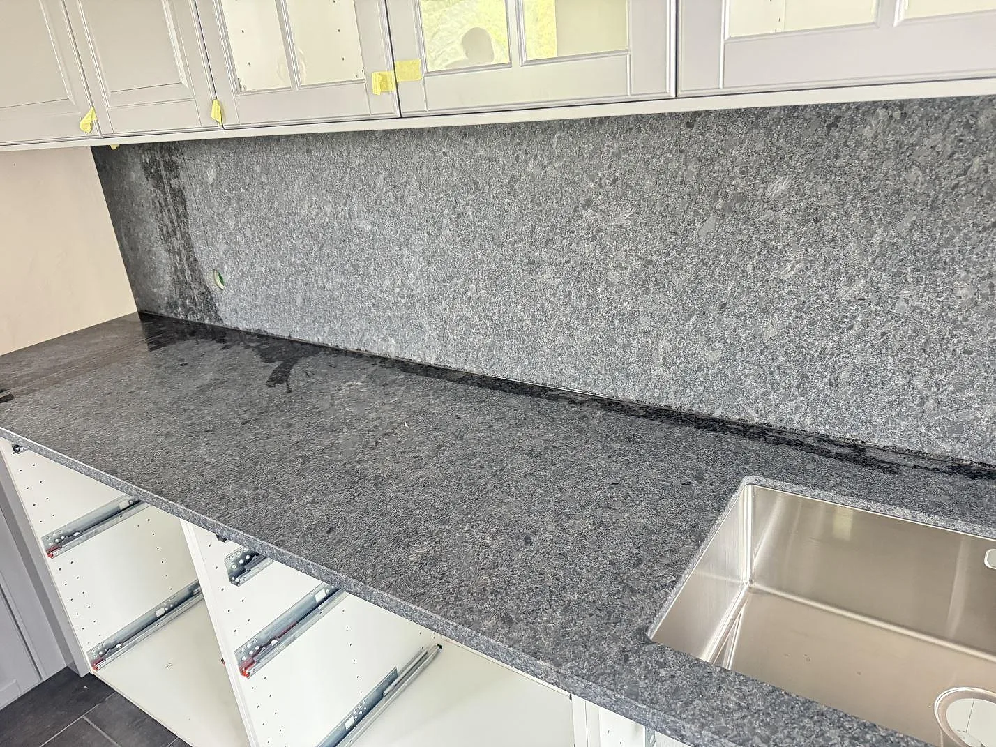 Lång köksbänkskiva i matt Steel Grey granit med diskho, öppen stomme och stänkskydd av sten i Löberöd.