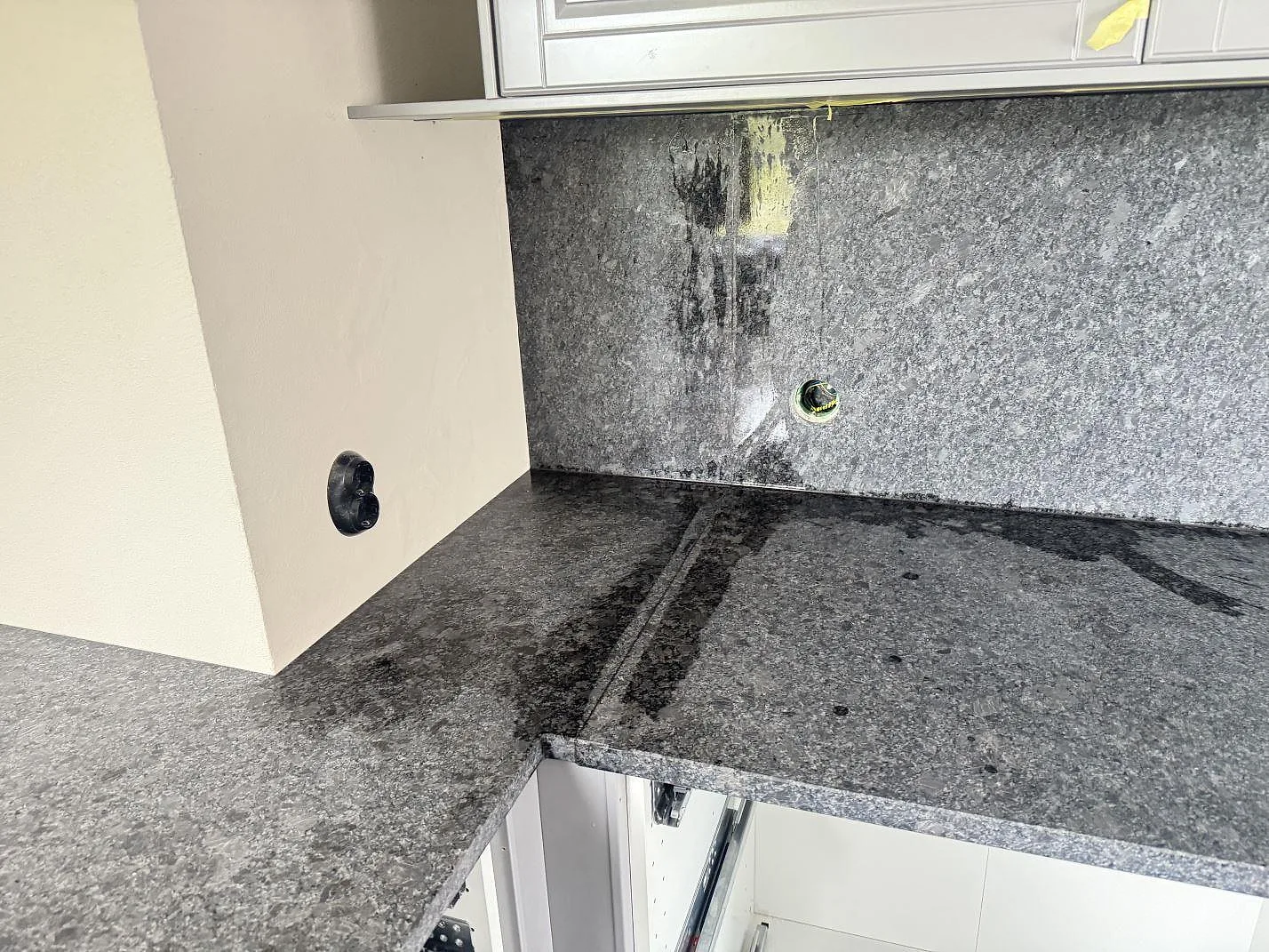 Hörn av köksbänkskiva i matt Steel Grey granit med stenklädd vägg och eluttag under montering i Löberöd.