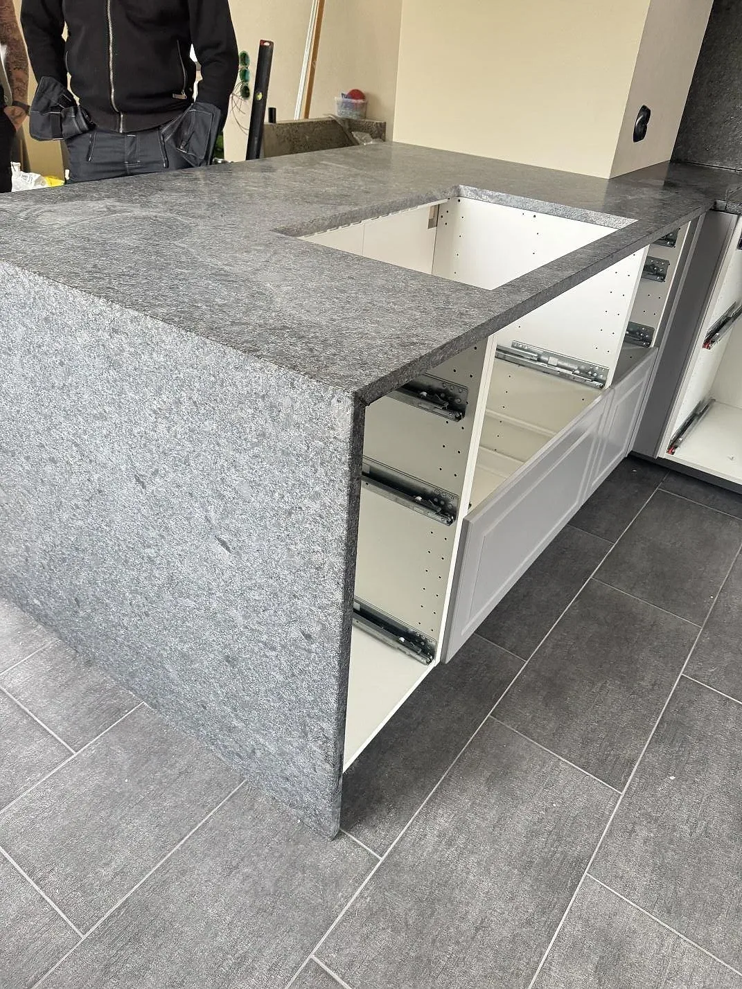 Sidovy av matt Steel Grey granit på köksödel med rektangulärt urtag och öppna skåpstommar i Löberöd.