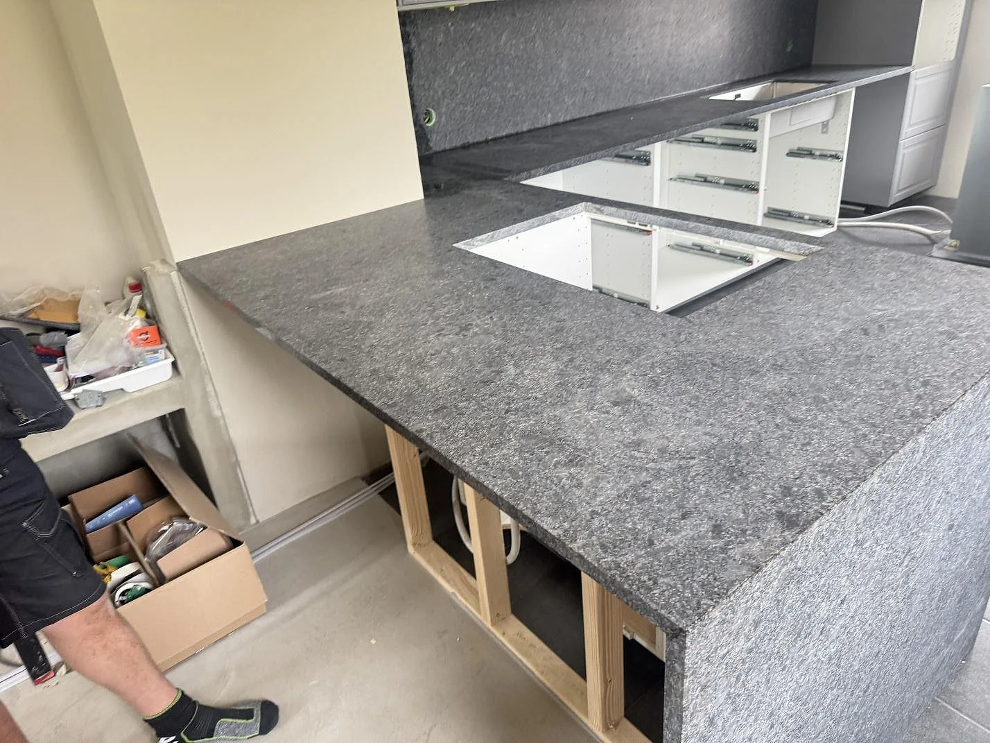 Större arbetsyta i matt Steel Grey granit med rektangulärt urtag och öppen trästomme i köket i Löberöd.