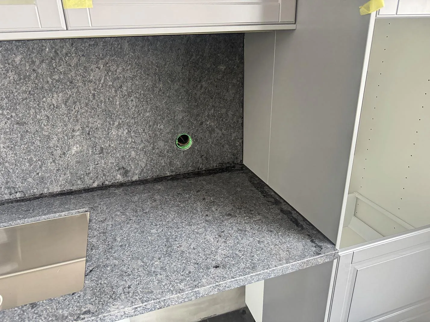 Detalj av matt Steel Grey granit som köksbänkskiva och väggbeklädnad runt diskhon i Löberöd.