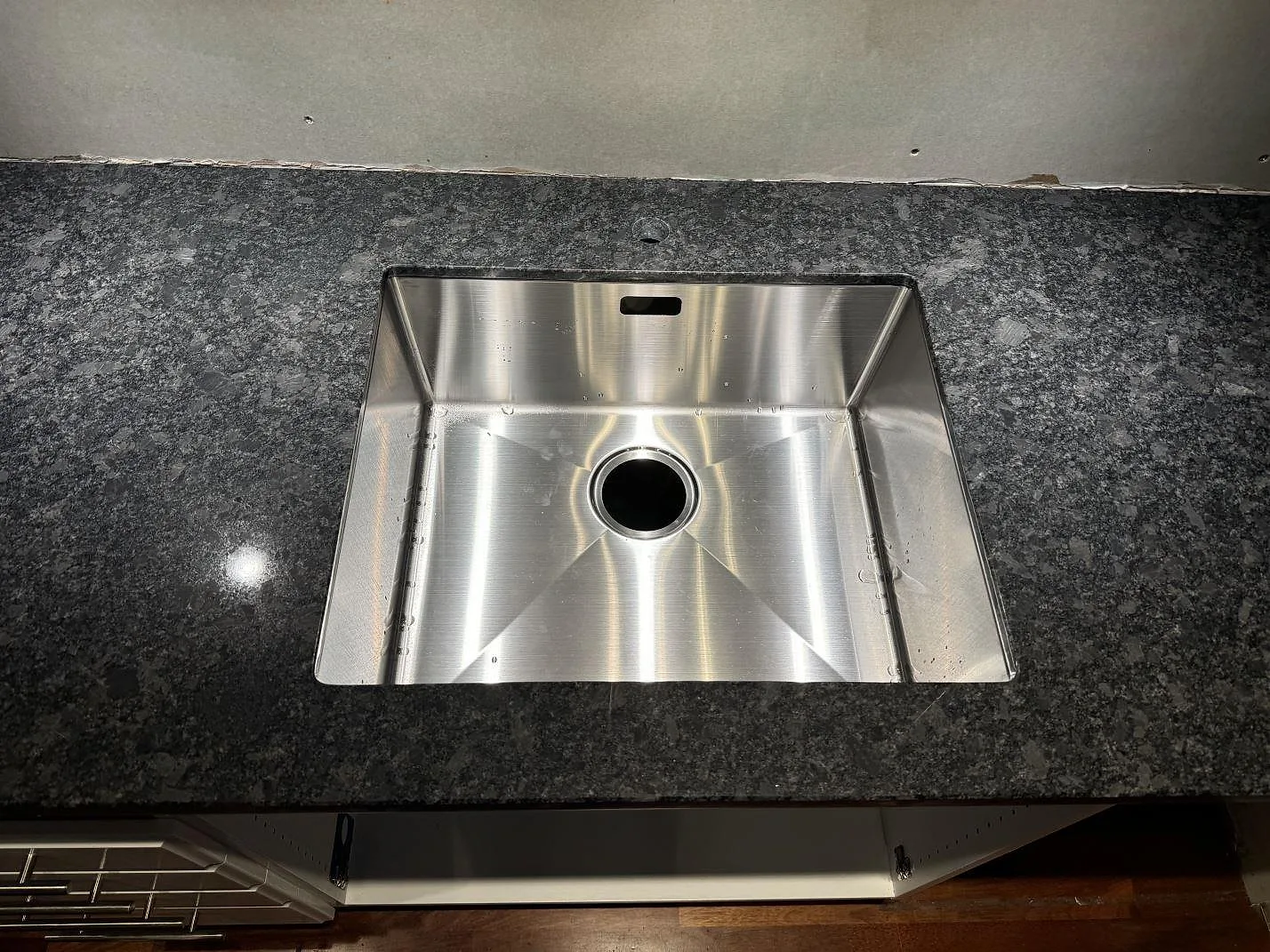 Närbild av rostfri diskho i polerad Steel Grey granit med mörkgrå kristallstruktur i ett kök i Lund.