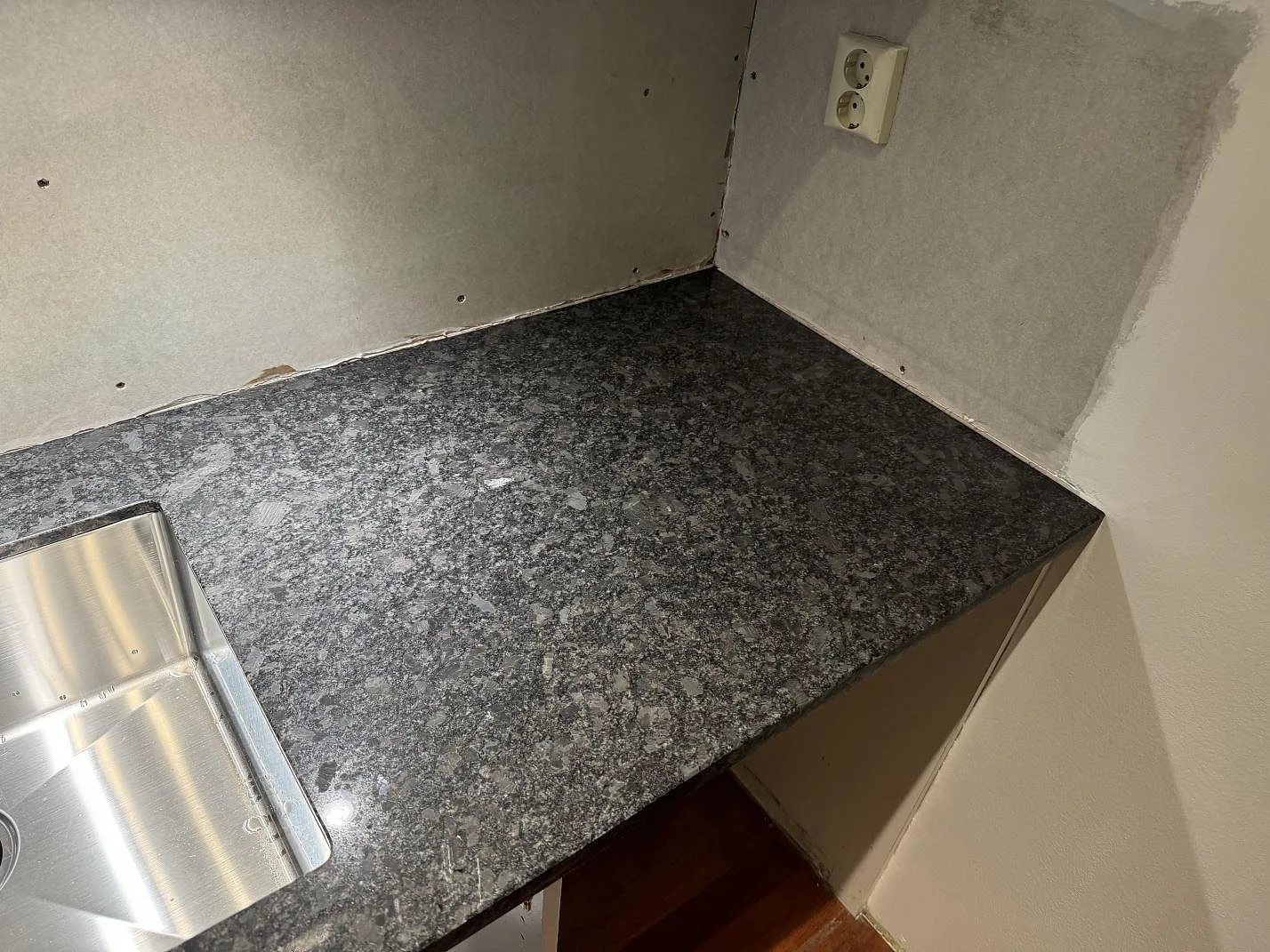 Hörndel av polerad Steel Grey granit vid rostfri diskho och ljus vägg i ett kök i Lund.
