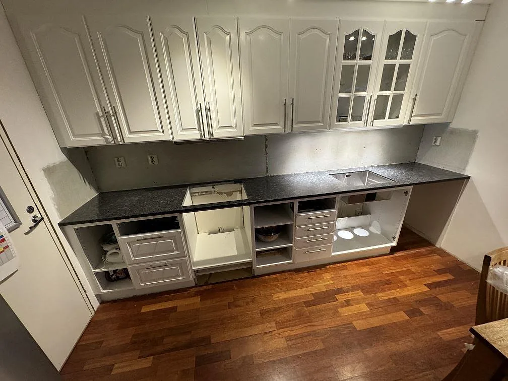 Kök i Lund med lång polerad bänkskiva i Steel Grey granit, rostfri diskho och öppna underskåp under montering.