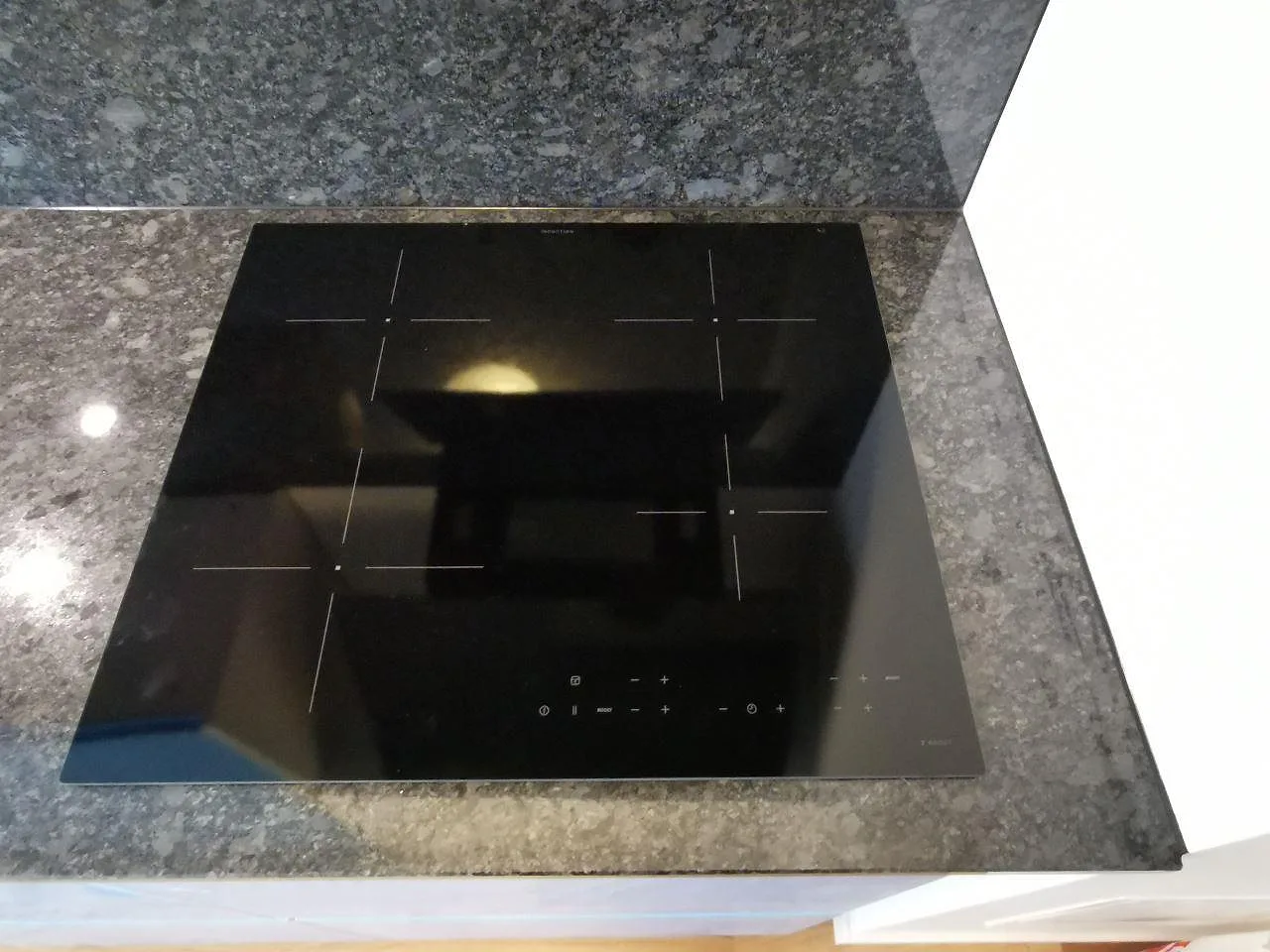 Polerad Steel Grey-bänkskiva i granit med infälld induktionshäll, sedd ovanifrån i ett kök i Malmö.