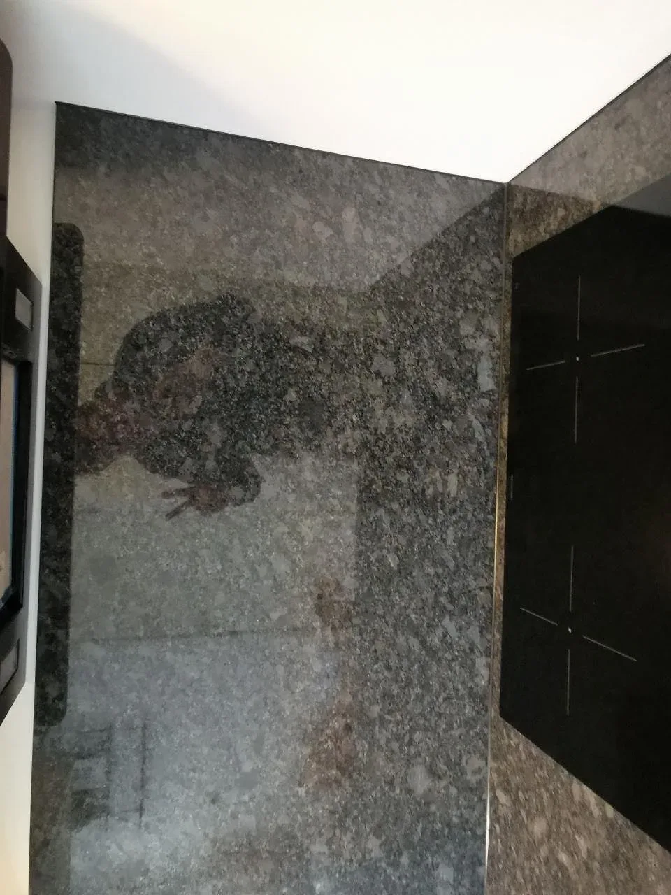 Stänkskydd och bänkskiva i polerad Steel Grey-granit kring induktionshällen i ett kök i Malmö.