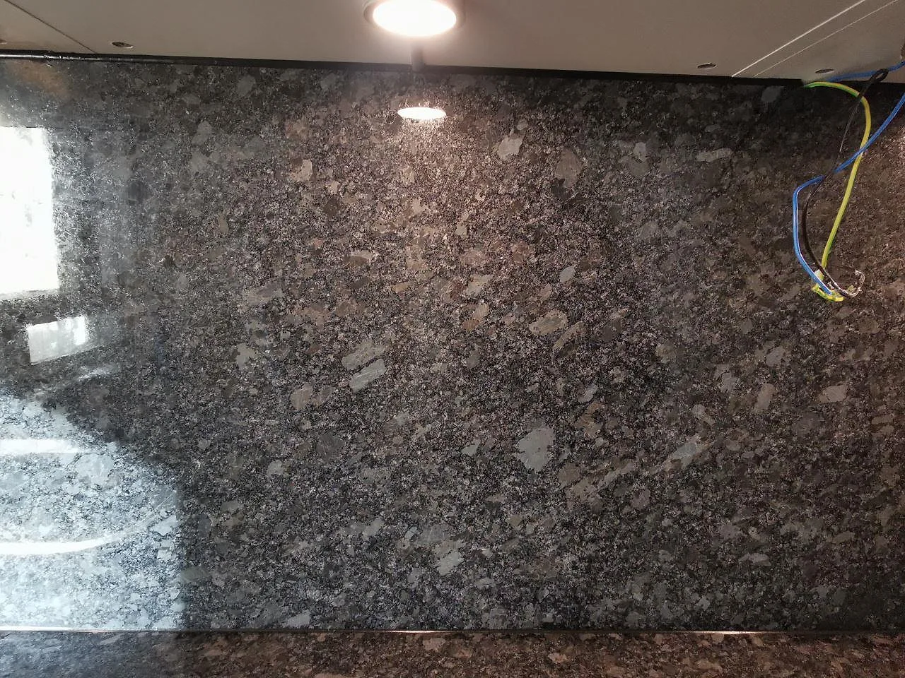 Uppvikt stänkkant i polerad Steel Grey-granit som följer köksbänkskivan i ett kök i Malmö.