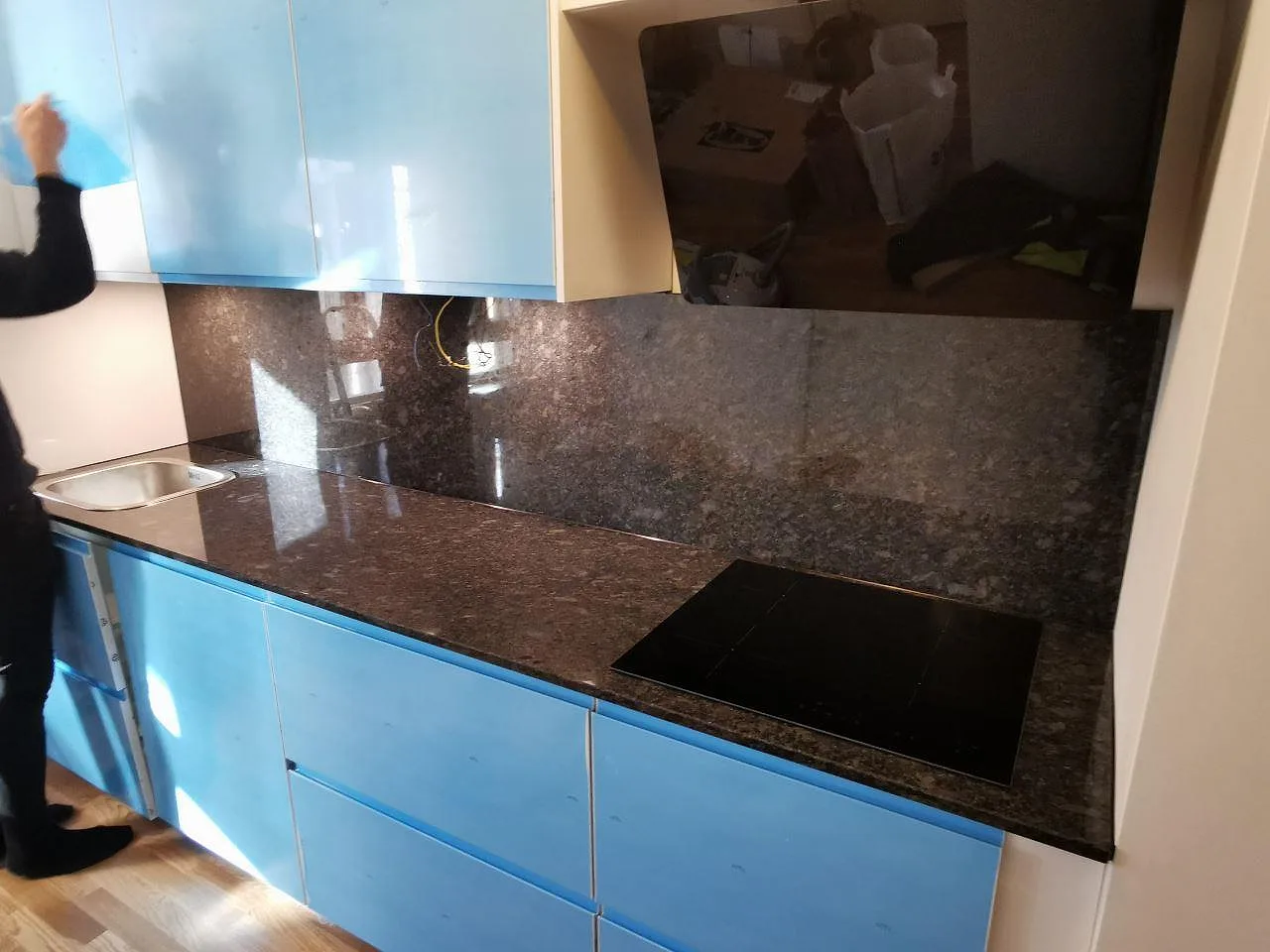 Köksbänkskiva i Steel Grey-granit, polerad, med uppvikt stänkkant och plats för induktionshäll mot ljusblå köksluckor i ett kök i Malmö.