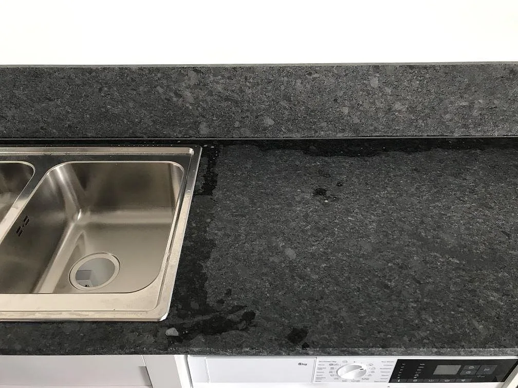 Detalj av rostfri diskho infälld i Steel Grey granit med matt yta och uppvikt stänkkant i ett kök i Malmö.
