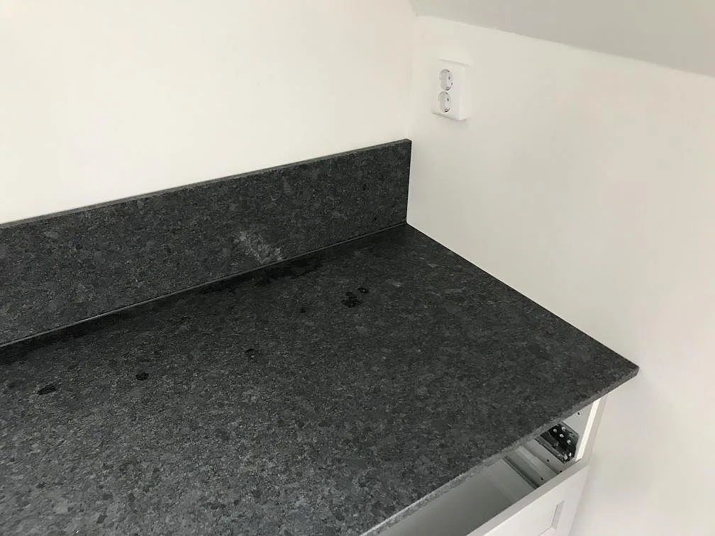 Köksbänkskiva i mörkgrå Steel Grey granit med uppvikt stänkkant mot vägg i ett kök i Malmö.