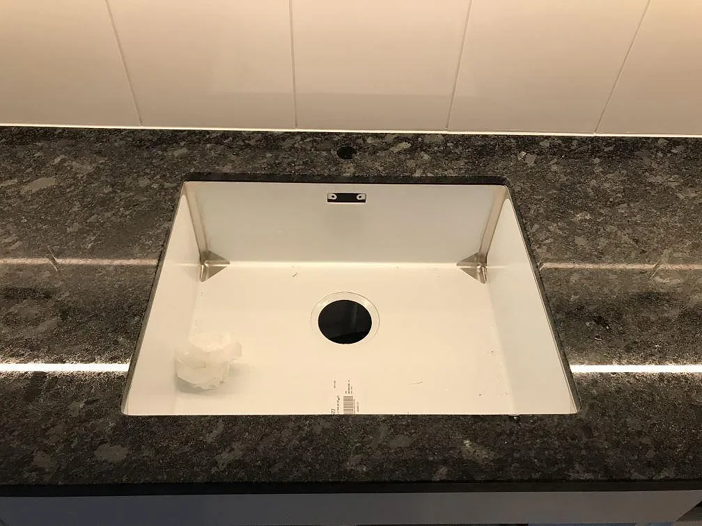 Vit underlimmad diskho monterad under en bänkskiva i Steel Grey granit i ett kök i Malmö.