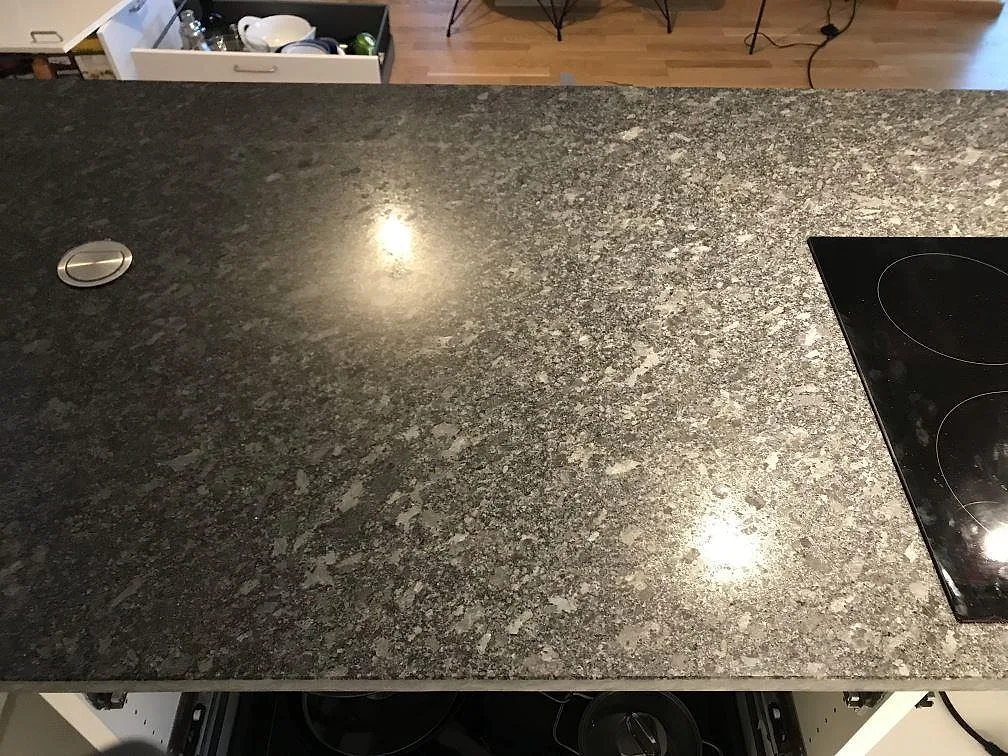 Polerad bänkskiva i Steel Grey granit med induktionshäll och speglande downlights i ett kök i Malmö.