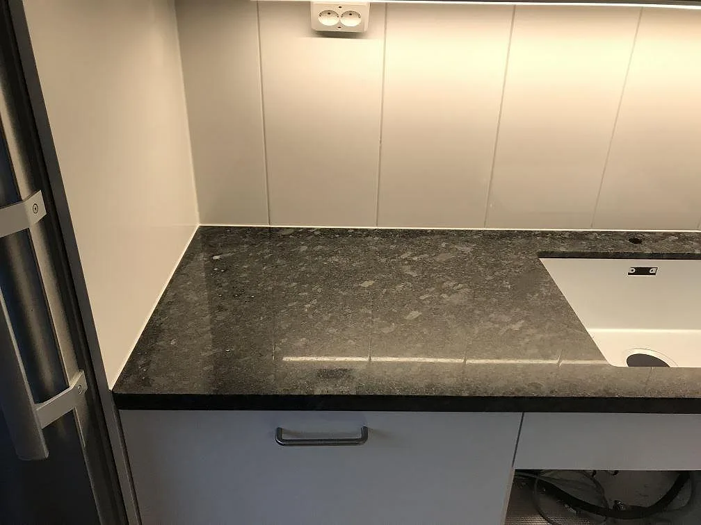 Köksbänkskiva i Steel Grey granit, polerad, monterad längs en vägg med vit underlimmad diskho i ett kök i Malmö.