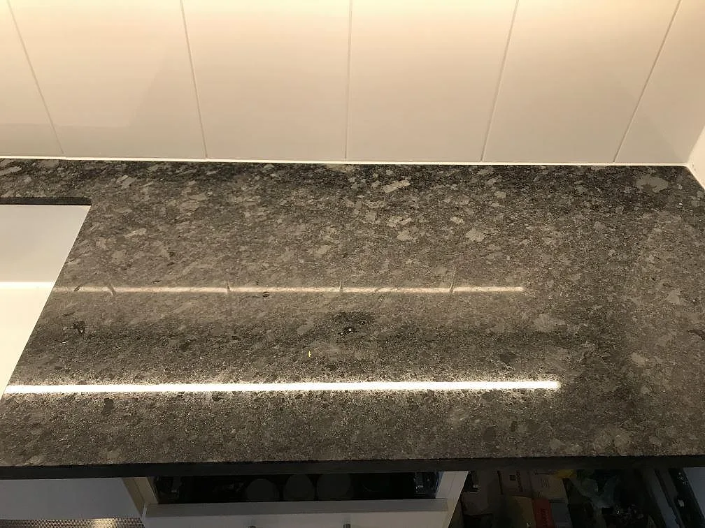 Bänkskiva i Steel Grey granit sedd uppifrån mot vitt stänkskydd i ett kök under montering i Malmö.