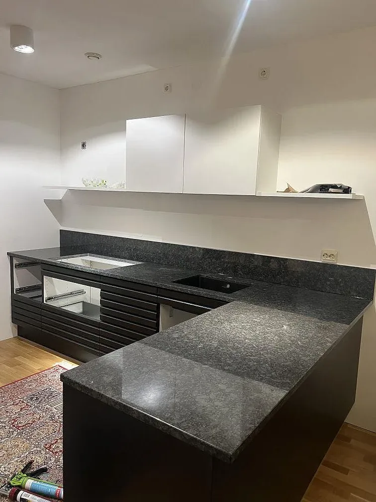 Köksö och väggbänk i polerad Steel Grey granit i ett öppet kök med vit skåpsinredning i Malmö.