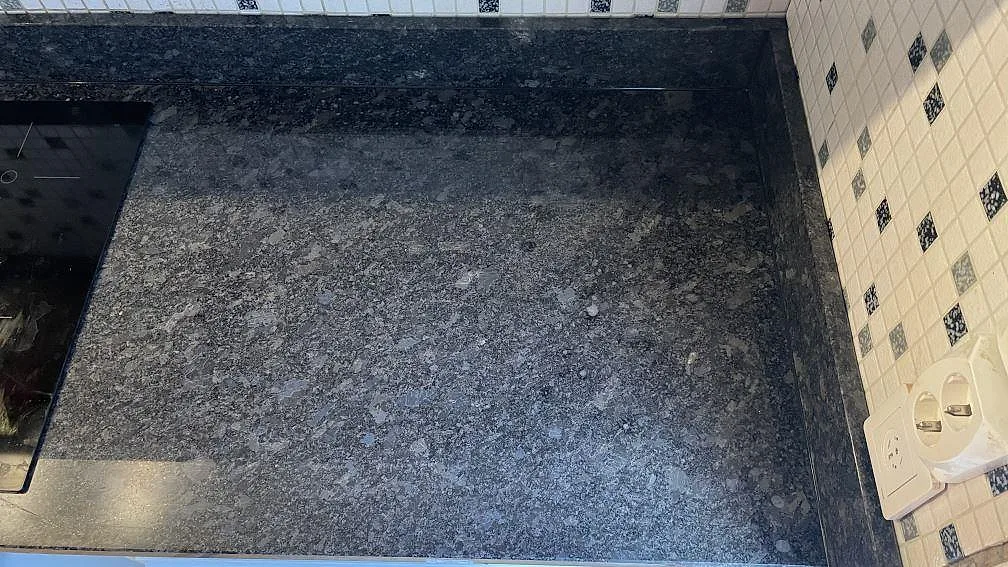 Hörn av Steel Grey granitbänk mot mosaikkaklad vägg i ett kök i Mölndal.
