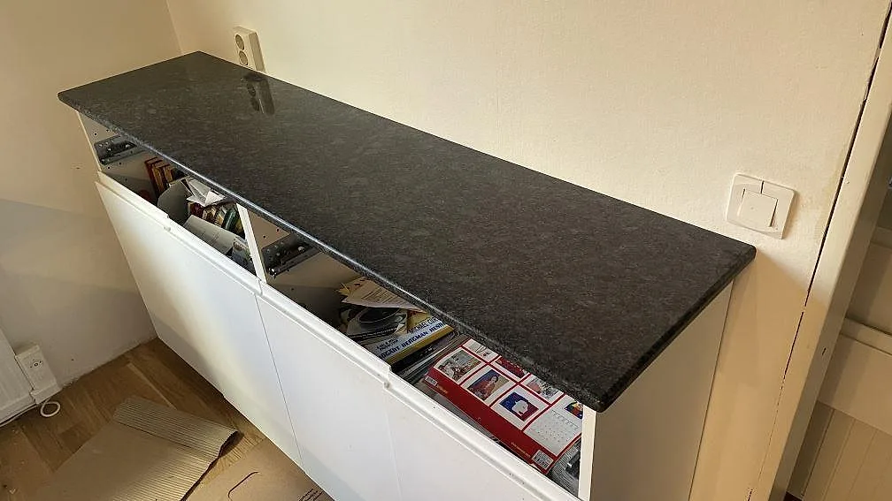 Bänkskiva i polerad Steel Grey granit ovanpå vit stomme i ett kök i Mölndal.