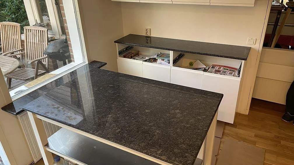 Köksö och bänkar i polerad Steel Grey granit med mörka skimrande inslag i ett kök i Mölndal, fotograferat under montering.