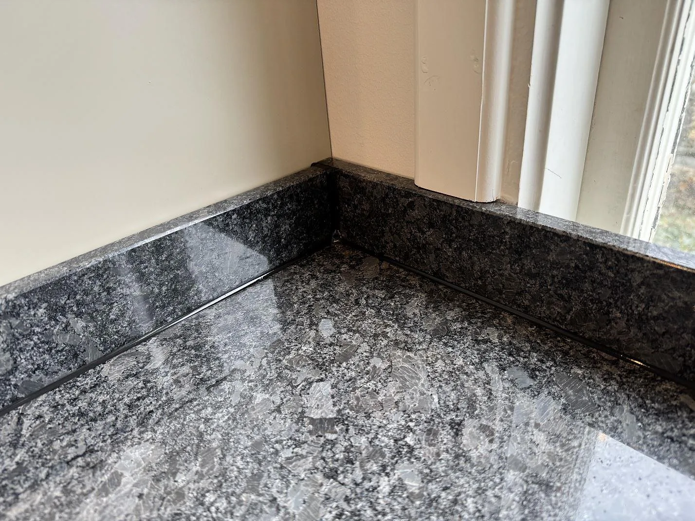 Detaljbild av polerad Steel Grey-granit med uppvikt stenkant i ett kök i Mölndal.