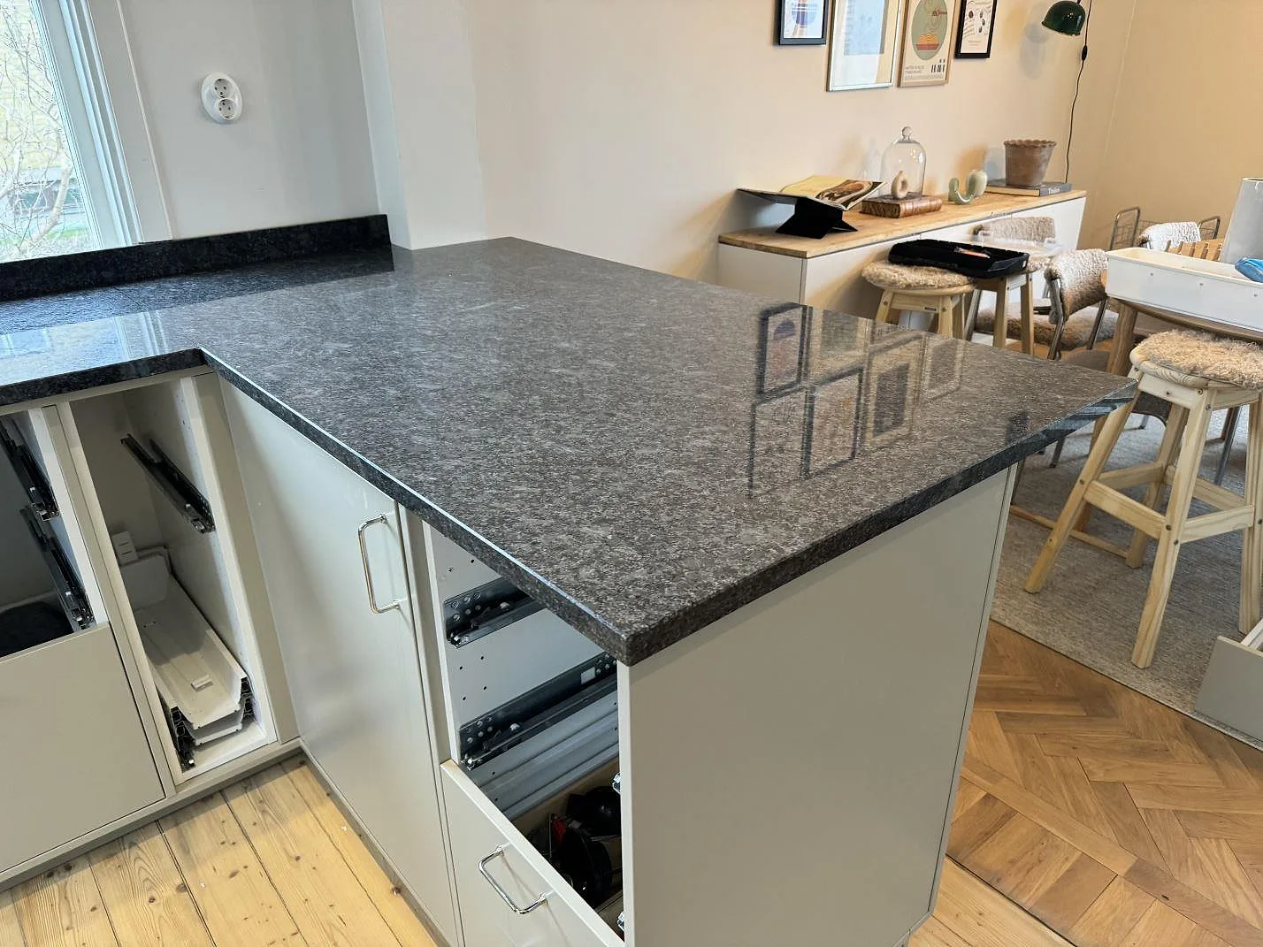 Köksbänkskiva i polerad Steel Grey-granit med halvö och vita köksstommar i ett kök i Mölndal.