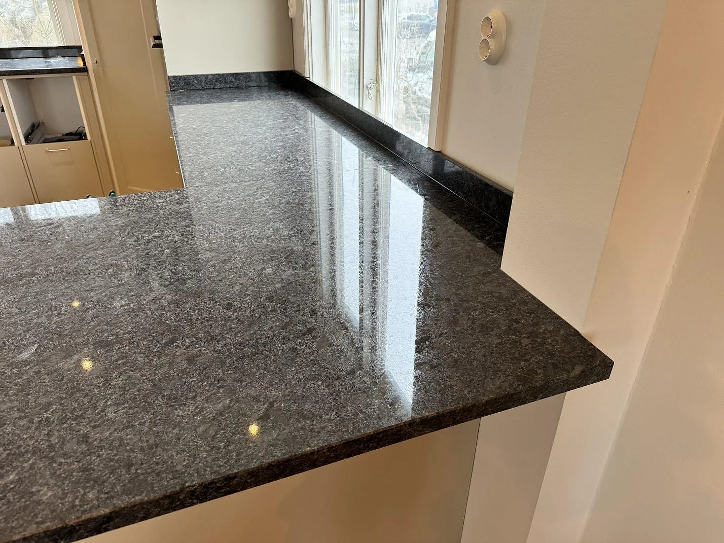 Polerad Steel Grey-granit som lång köksbänk vid fönster och halvö i ett kök i Mölndal.