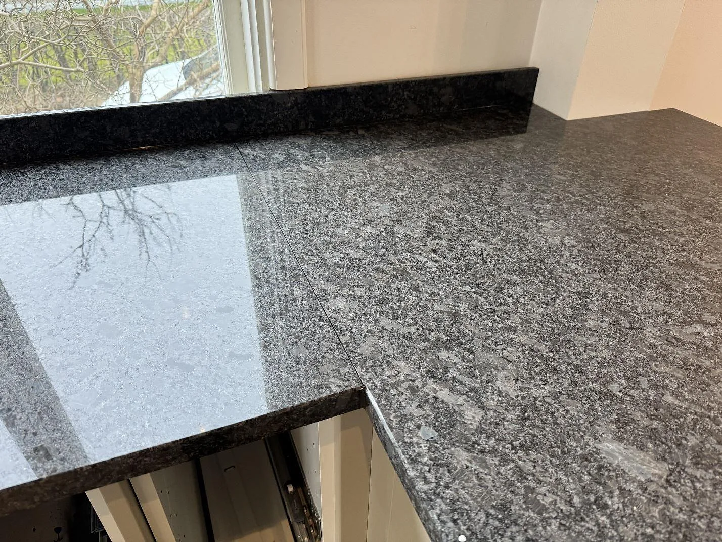 Närbild på skarven mellan två polerade Steel Grey-bänkskivor och låg stenkant vid fönster i Mölndal.