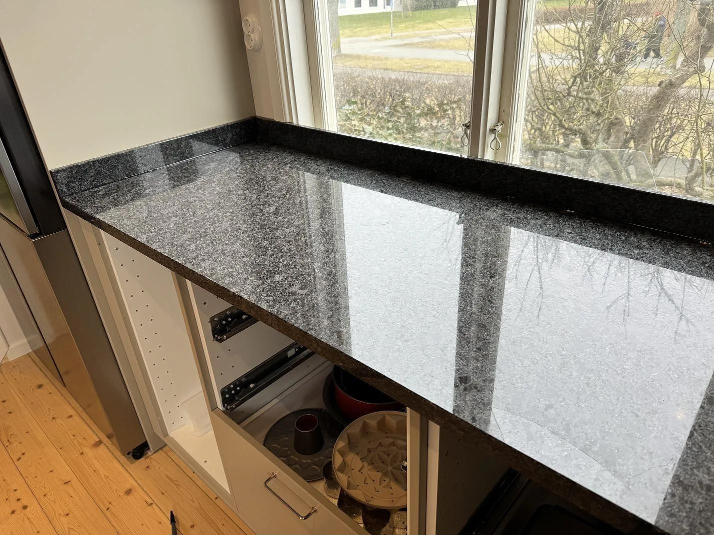 Polerad Steel Grey-granit som arbetsbänk under fönster med mörk stenkant i ett kök i Mölndal.