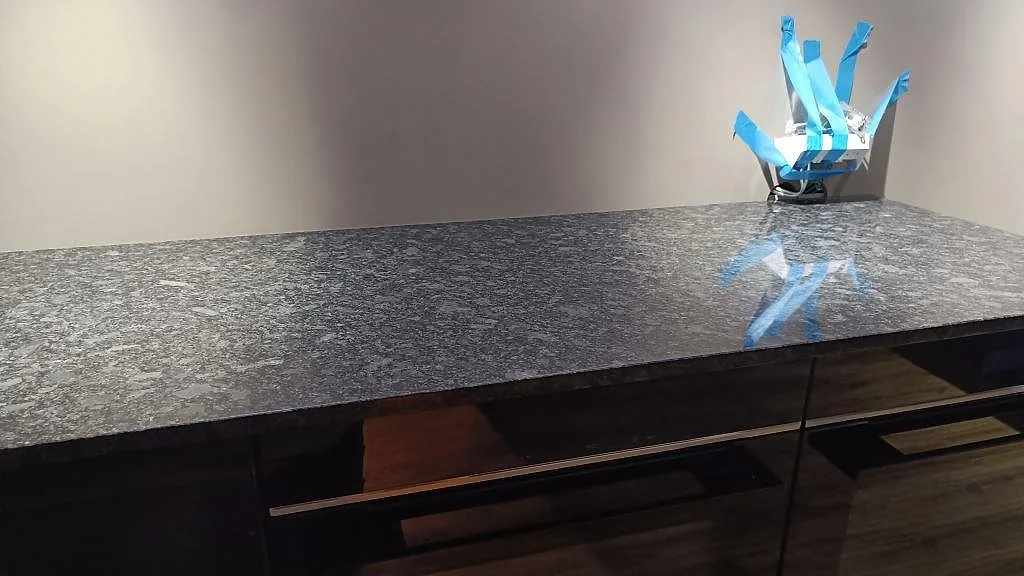 Detaljbild av köksbänkskiva i polerad Steel Grey granit med synlig stenstruktur och arbetsbelysning i Nybro.