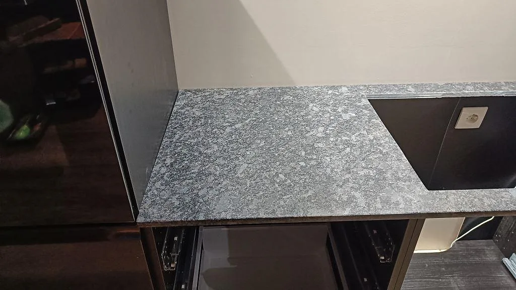 Köksbänkskiva i polerad Steel Grey granit med rektangulär öppning i stenen och mörka stommar i Nybro.