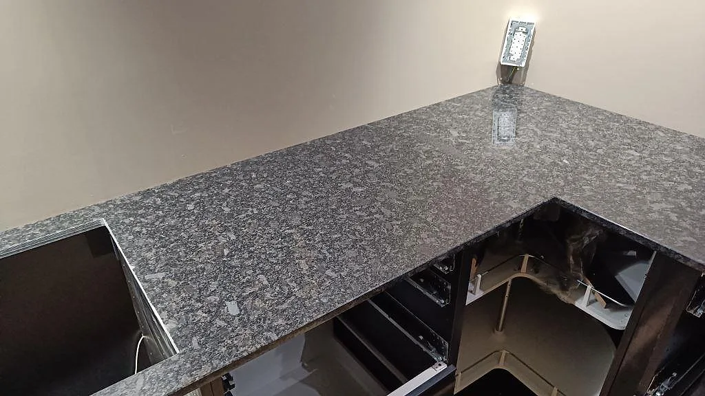 L-formad köksbänkskiva i polerad Steel Grey granit med grå flammig yta i ett kök i Nybro.
