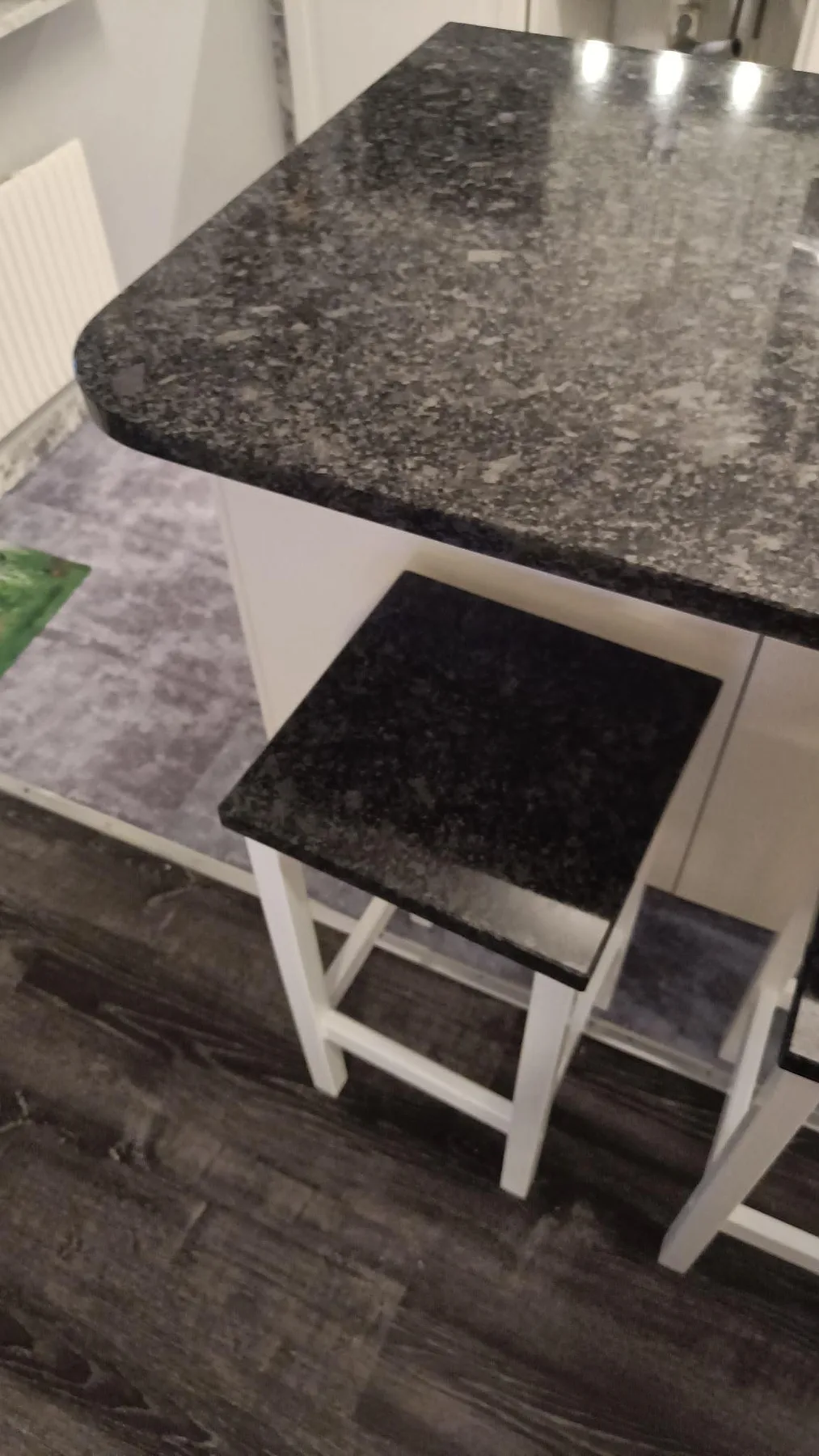 Detalj av rundat hörn på köksö i polerad Steel Grey granit med barstol under skivan i Oxie.