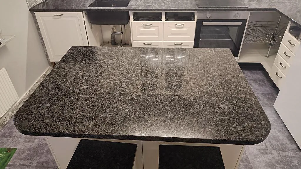 Stor köksö i polerad Steel Grey granit med rundade hörn och synlig väggbänk i ett kök i Oxie.
