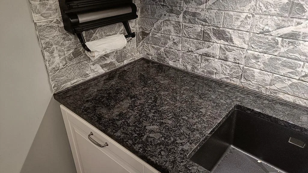 Polerad Steel Grey granit vid underlimmad mörk diskho och grå stenplattelik backsplash i Oxie.