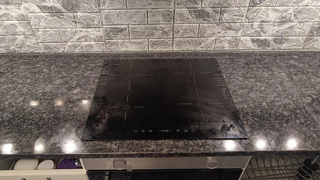 Infälld häll i polerad Steel Grey granit med grå stenplattelik backsplash i ett kök i Oxie.