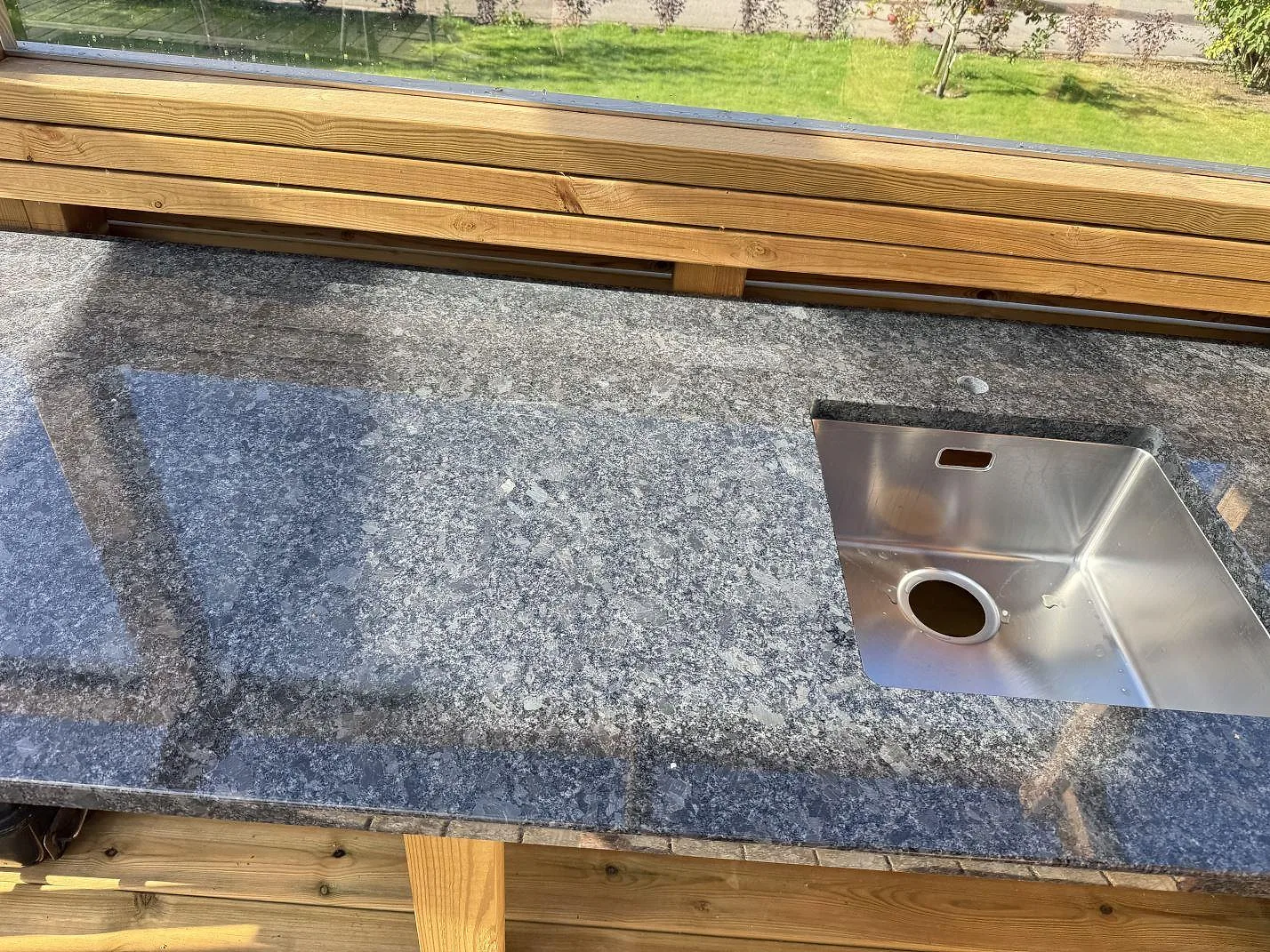 Lång arbetsyta i Steel Grey granit med rostfri diskho vid fönsterparti i ett utekök i Ramlösa.