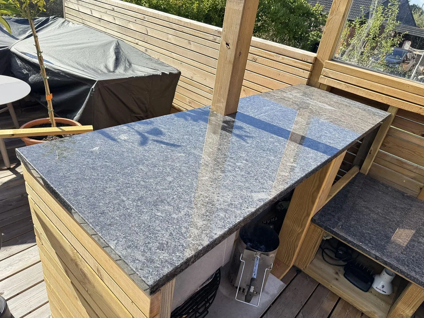 Sidovy av en monterad bänkskiva i Steel Grey granit runt en trästolpe i ett utekök i Ramlösa.