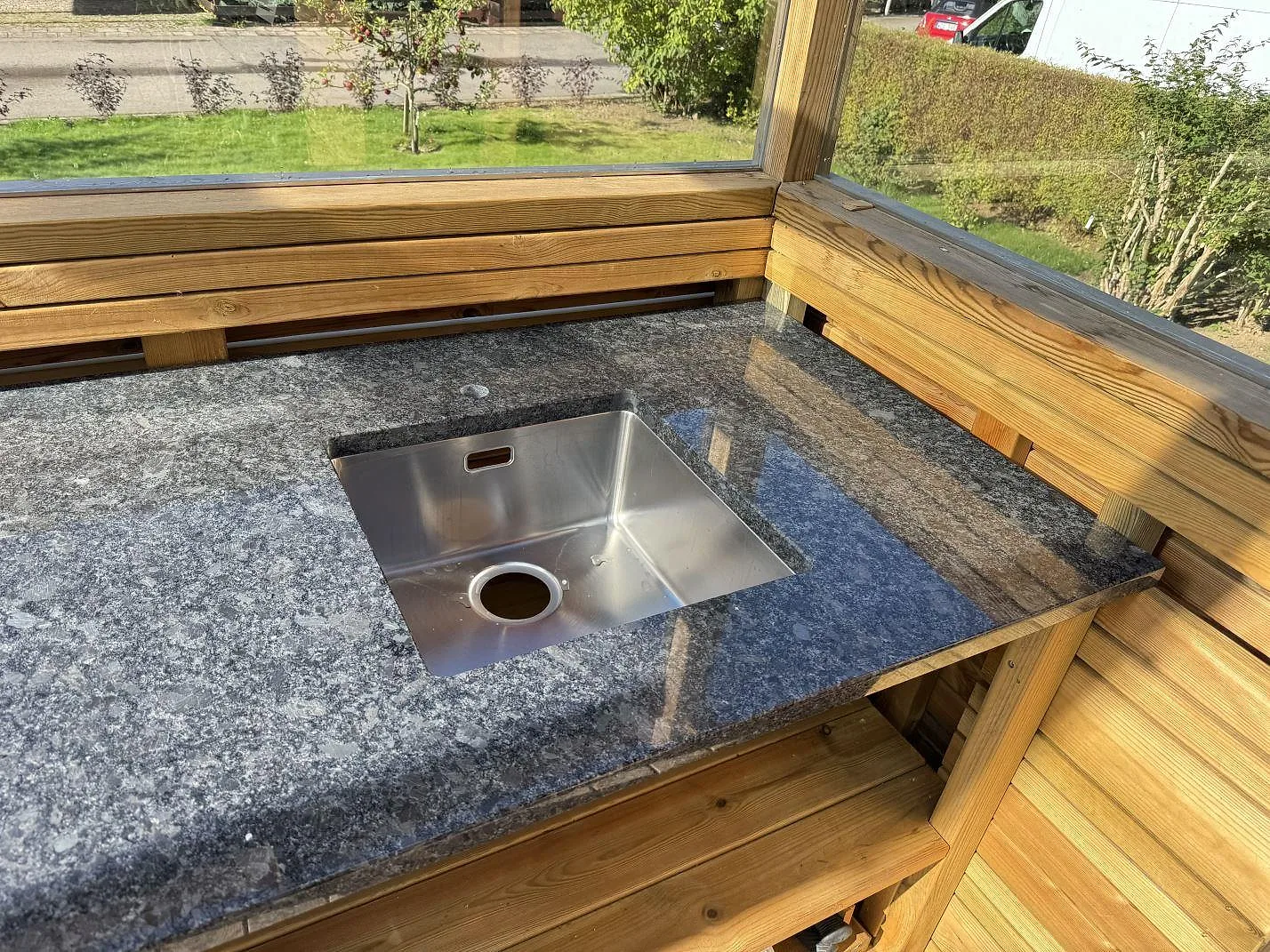 Närbild på Steel Grey granit som köksbänkskiva med rostfri diskho och träinredning i Ramlösa.