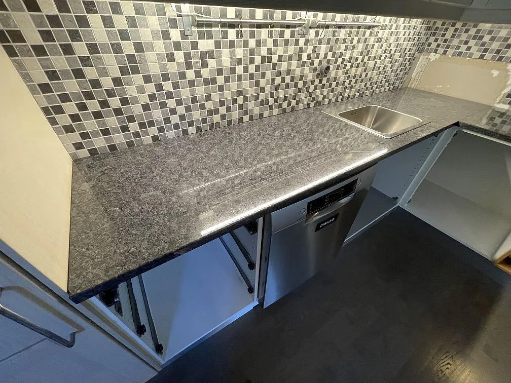 Polerad köksbänkskiva i Steel Grey granit med synlig diskho och lång arbetsyta i ett kök i Saltsjö boo.