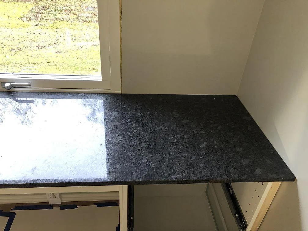 Köksbänkskiva i Steel Grey granit monterad längs fönstervägg i ett kök under installation i Södra Rörum.