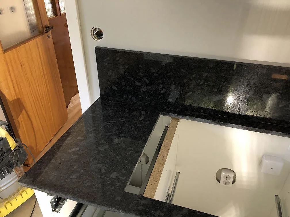 Köksbänkskiva i Steel Grey granit med uppvikt stänkkant och urtag för diskho, monterad i ett kök i Södra Rörum.