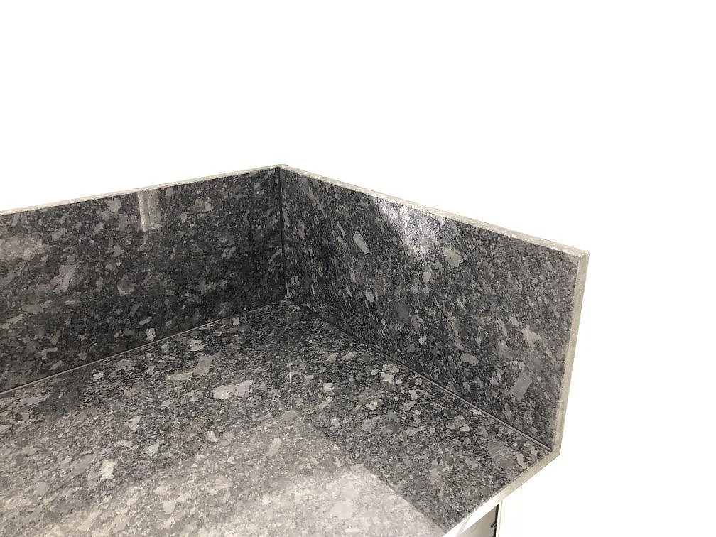 Detalj av köksbänkskiva i Steel Grey granit med uppvikt stänkkant i hörnet i ett kök i Södra Rörum.