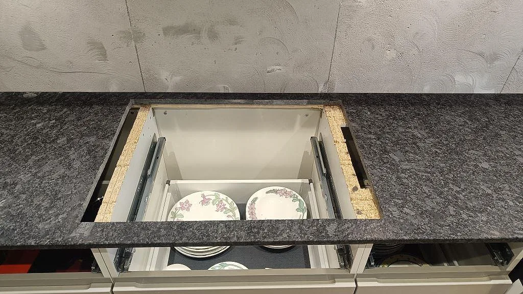 Detalj av matt Steel Grey granit runt öppning i bänkskivan på vita köksstommar i Staffanstorp.