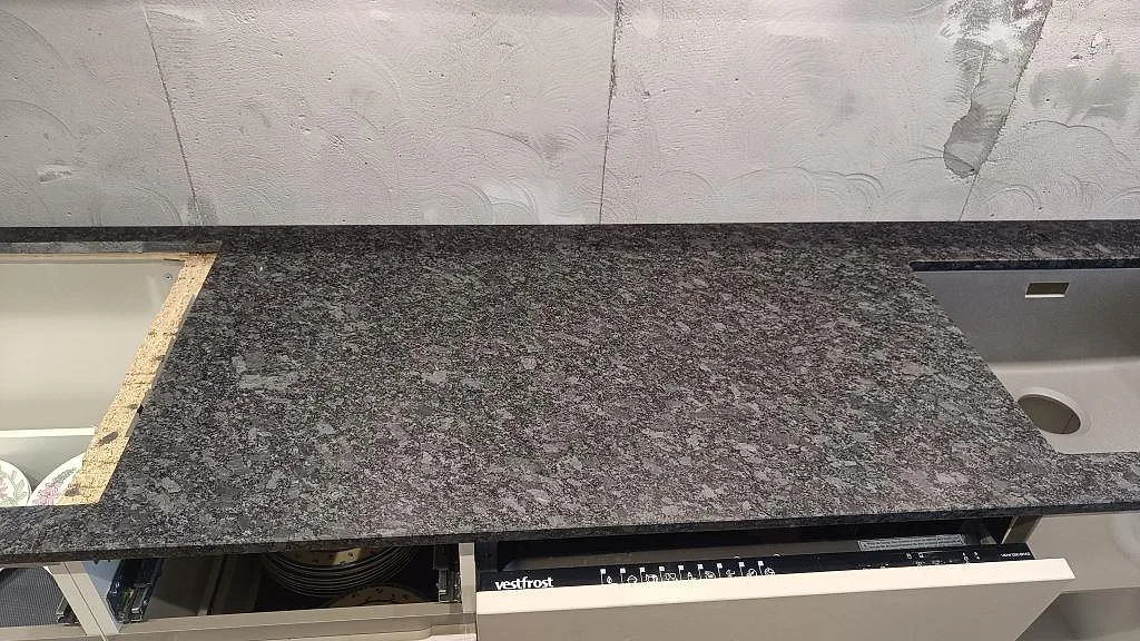 Närbild av matt Steel Grey granitbänkskiva med diskho och öppen skåpstomme i Staffanstorp.