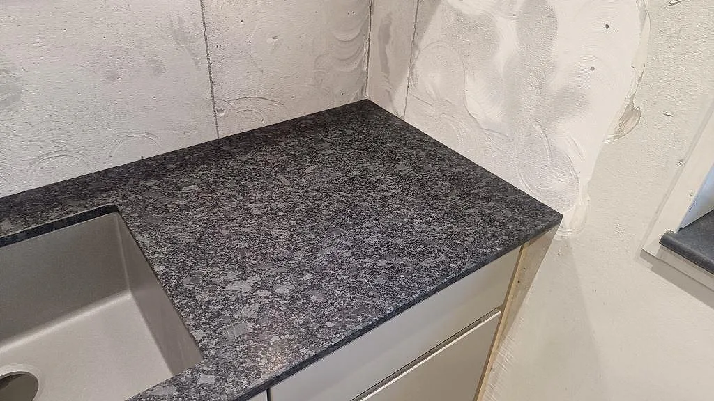 Hörn vid diskhon med matt Steel Grey granit och rå väggyta under köksmontering i Staffanstorp.