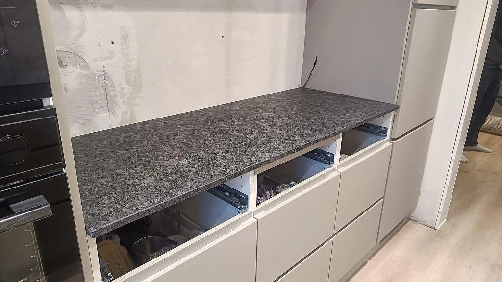 Rak köksbänkskiva i matt Steel Grey granit på vita skåpstommar under montering i Staffanstorp.