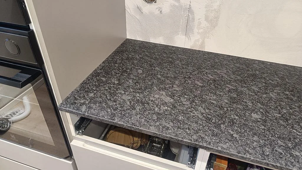 Rak bänkskiva i matt Steel Grey granit intill inbyggnadsugn under köksmontering i Staffanstorp.