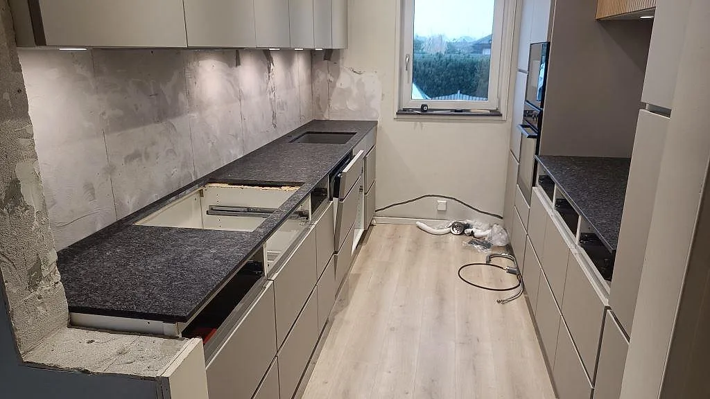 Köksbänkskiva i matt Steel Grey granit med L-formad bänkdel och rak bänkrad i ett kök i Staffanstorp.
