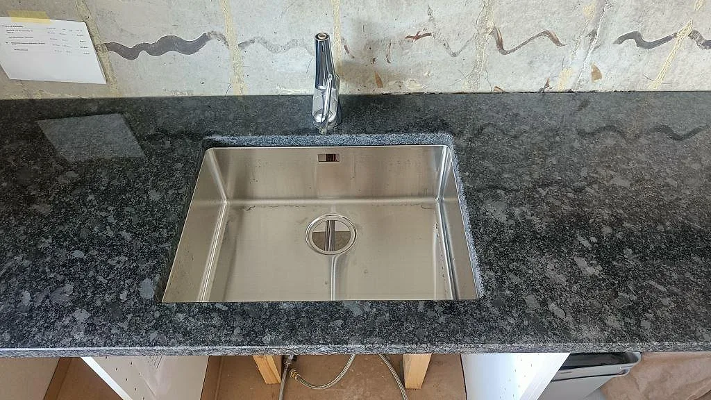 Närbild på underlimmad rostfri diskho i en köksbänkskiva av Steel Grey granit i Staffanstorp.